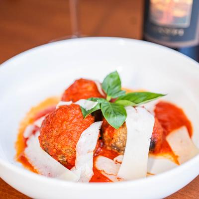 Meatballs served in a tomato sauce and topped with shaved cheese and fresh basil.