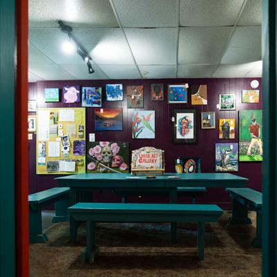 Gallery room with colorful paintings and teal seating.