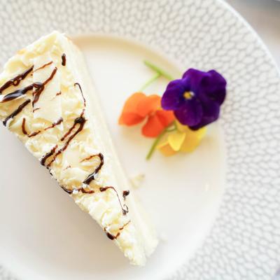 Chocolate-drizzled cheesecake slice served on a patterned white plate with flower garnish.