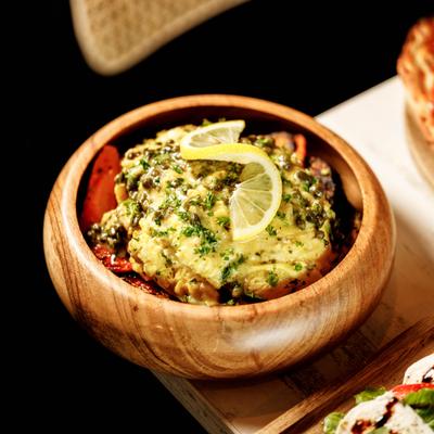 A wooden bowl holds a creamy dish topped with capers and lemon.