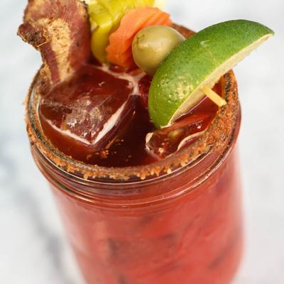 Bloody Mary garnished with bacon, pickled veggies, olive, and lime wedge\.