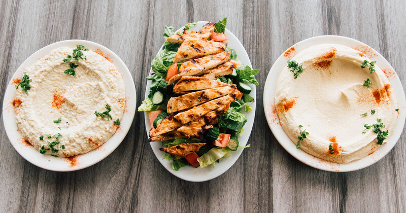 Grilled chicken salad in the middle, two plates with spreads on both sides