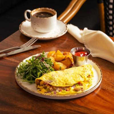 Omelet with sausage and peppers served with potatoes, arugula salad, and a cup of coffee.