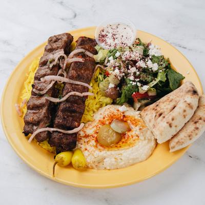 Grilled kebab served over yellow saffron rice with sides of hummus, pita and a salad.