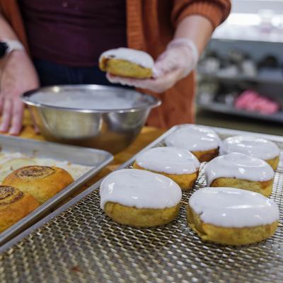 A person icing cinnamon rolls on a wire rack.
