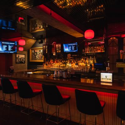 Bar counter lined with leather stools beneath red pendant lights.
