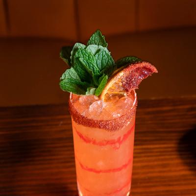 A cocktail with ice in a glass with spiced rim, mint and orange garnish.