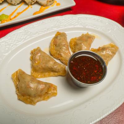 Steamed dumplings served on a white, oval sauce with a side of dipping sauce.