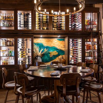 A round table with chairs set in front of a wall with a wine rack and hard liquor locker.