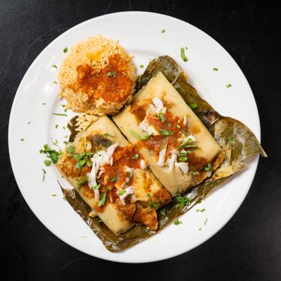 Banana leaf wrapped tamales served with red salsa, cheese, and Mexican red rice.