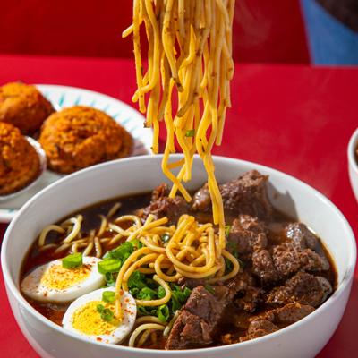 Noodles being lifted from a bowl of beef noodle soup.