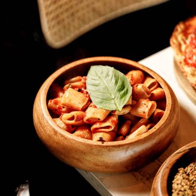 A wooden bowl of rigatoni pasta with red sauce and basil leaf.