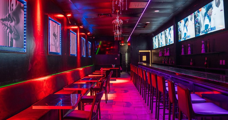 Interior, tables, a long bar, chandeliers, and multiple televisions showing a sports broadcast