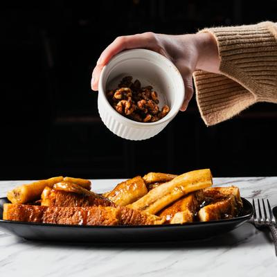A person adds candied walnuts to Bananas faster french toast, hand shot.