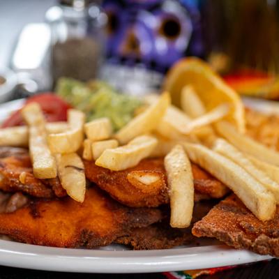 Close-up of breaded and fried chicken cutlets served with fries and guacamole.
