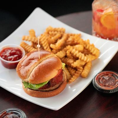 Chicken sandwich served with fries and dipping sauce, alongside a cocktail.