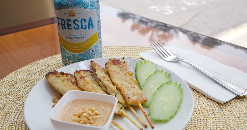 Chicken satay skewers with peanut sauce and slices of cucumber