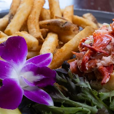 Close-up of a lobster roll with fries and orchid garnish.