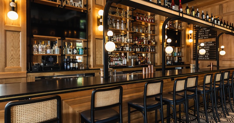 A stylish bar interior - a black countertop, wooden accents and shelves stocked with liquor bottles