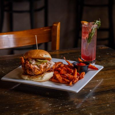 Nashville hot chicken sandwich with sweet potato fries and a cocktail.