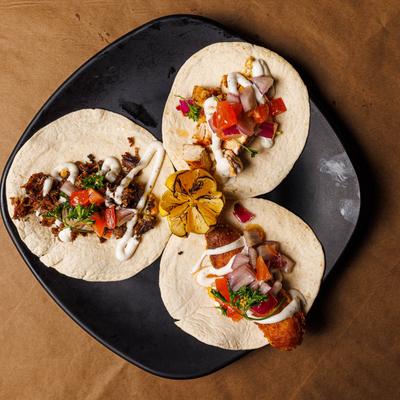 Three tacos with different toppings on a black plate.