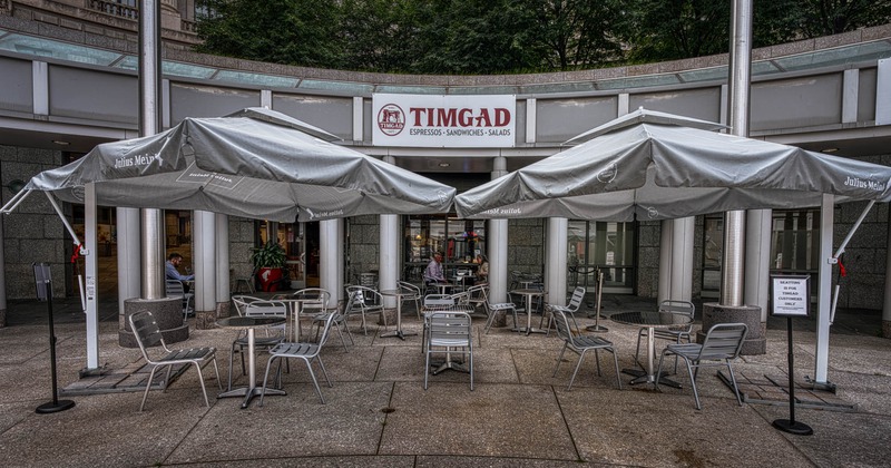Exterior, partially covered seating area, tables and chairs under large parasols, restaurant front