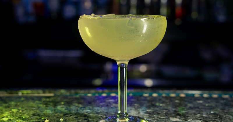 A yellow cocktail drink on a bar counter, side view