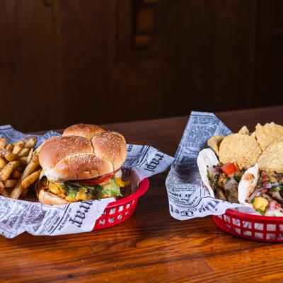 Burger and tacos served in red plastic baskets lined with newspaper-print paper.