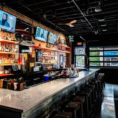 Interior with with a long bar counter and multiple television screens.