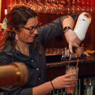 A bartender pouring a glass of drink.
