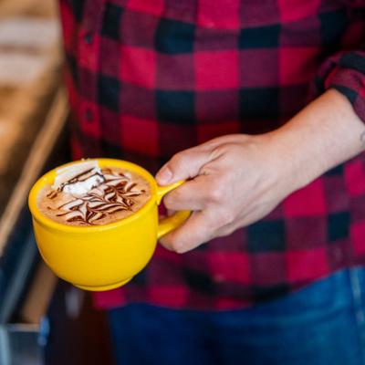 A barista  holds a mug of coffee at a coffee bar counter.