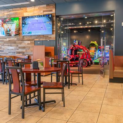 Dining area with TVs and an arcade room in the background.