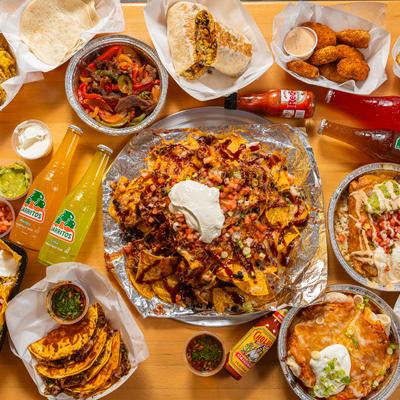 An array of Mexican dishes and soda bottles on a wooden table.