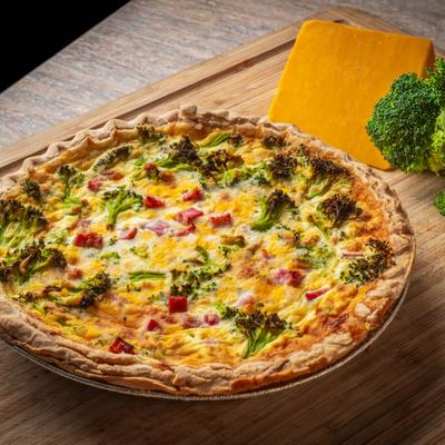 Broccoli Ham and Cheese quiche served on a wooden board with a cheddar block and broccoli.