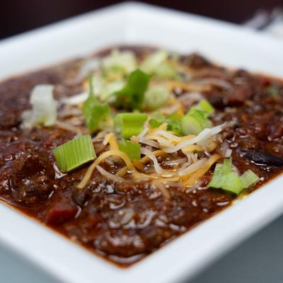 Bowl of chili topped with scallions and grated cheese, close-up.