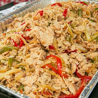 Shredded chicken with green and red peppers arranged on a catering tray.