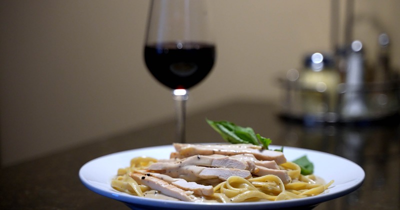 Fettuccine Alfredo featuring sliced chicken breast, alongside a glass of wine