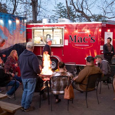 People sitting around a fire pit near a red food truck.