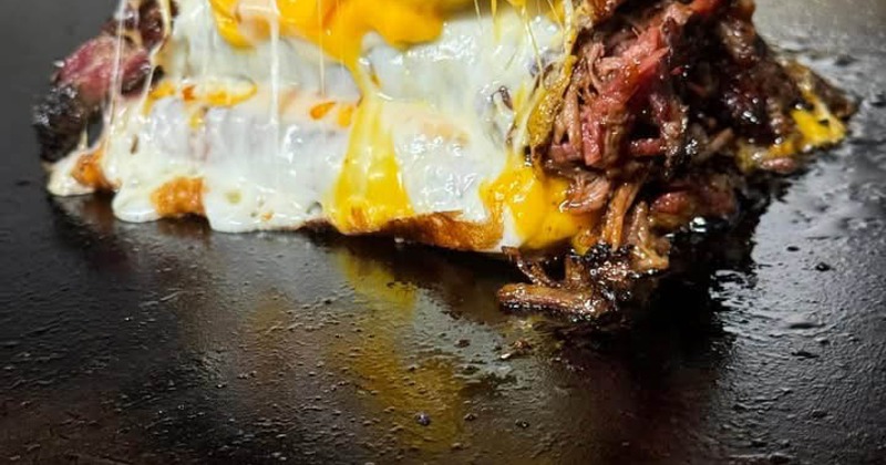 A brisket grilled cheese sandwich being prepared on a griddle