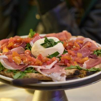 A gourmet pizza topped with burrata cheese, prosciutto, and tomatoes.