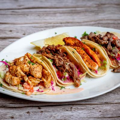 Steak taco, salmon taco, pork taco, and chicken taco on a white plate.