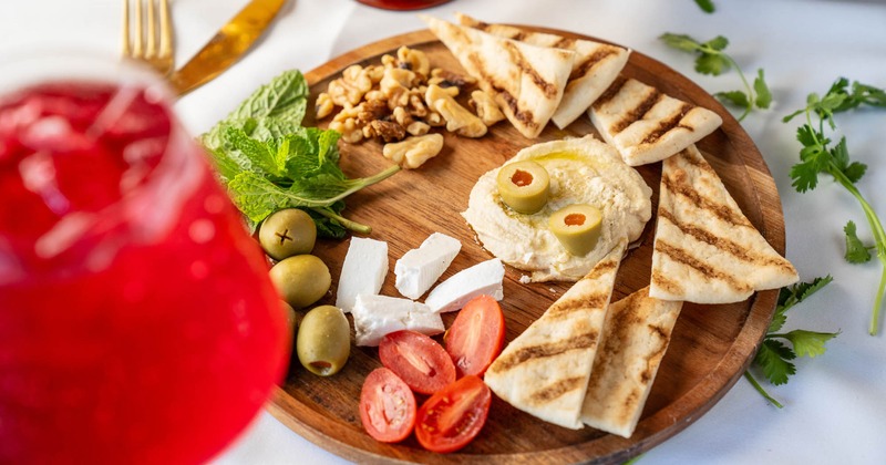Hummus board with pita, walnuts, feta, grape tomatoes, olives, and mint leaves