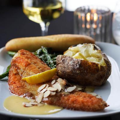 Breaded fish fillet with a baked potato, green beans, almonds, and sauce.
