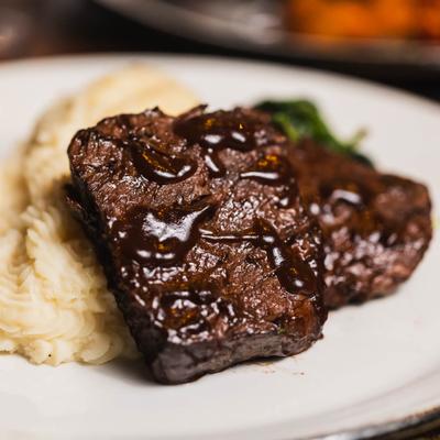 Braised beef drizzled with dark sauce, served with a side of creamy mashed potatoes.