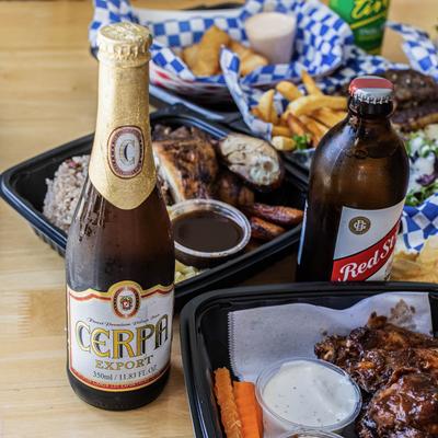 A table set with various foods including barbecue wings, fries, burgers, and bottles of beer.