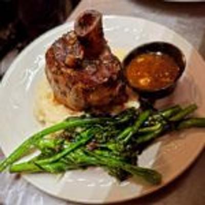 A plate featuring a succulent lamb shank with creamy mashed potatoes, broccolini, and sauce.