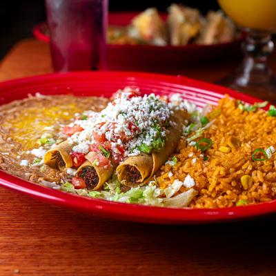 Flautas served with refried beans and rice, garnished with queso fresco.