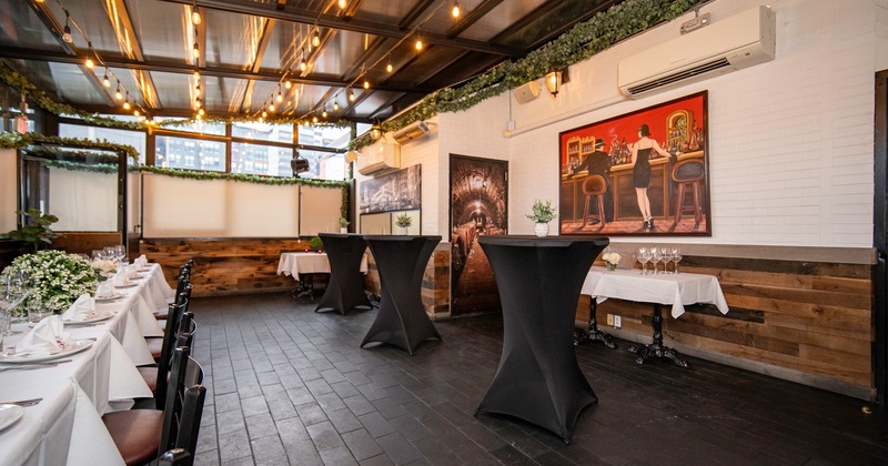 An elegant dining setup in an enclosed patio space with a set dining table and tall cocktail tables