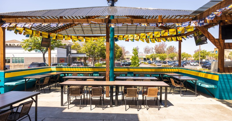Outdoor seating area under a pergola with tables, chairs, and beer banners.