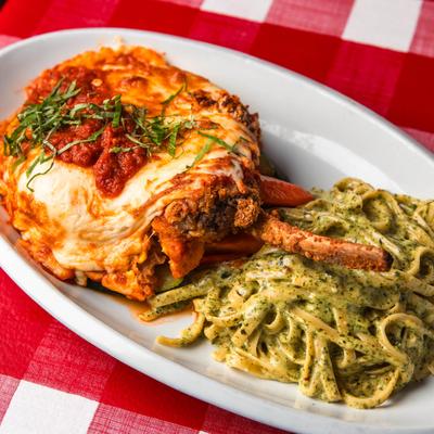 Veal Chop Parmigiana served with pesto pasta on a white plate, set on a red checkered tablecloth.